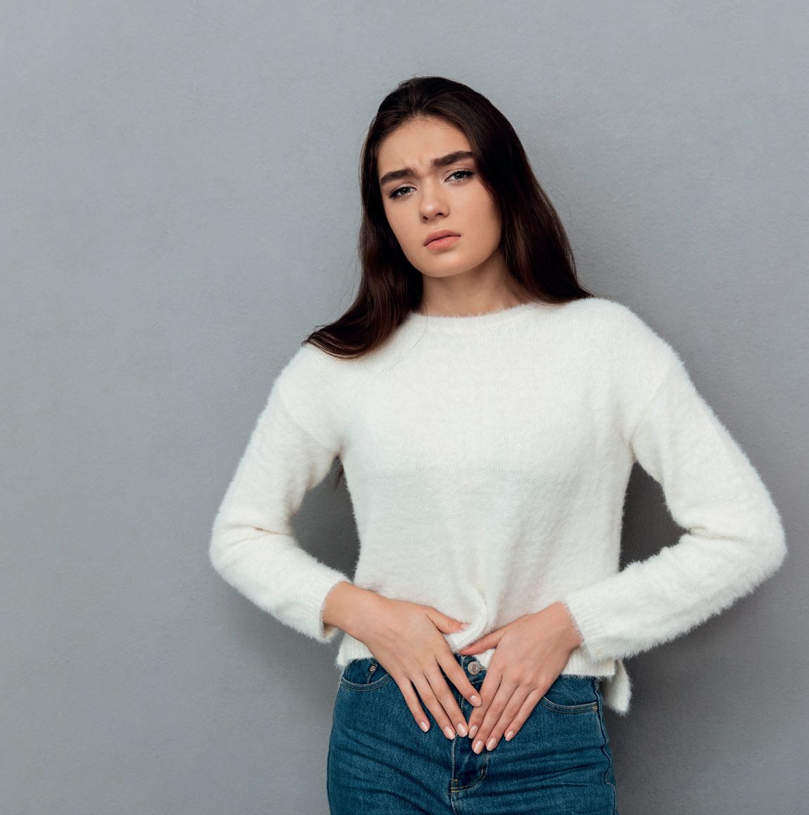 Mulher jovem com as mãos sobre o baixo-ventre, com expressão de desconforto