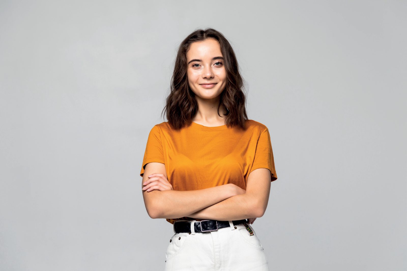 Mulher jovem sorrindo de braços cruzados, de camiseta laranja