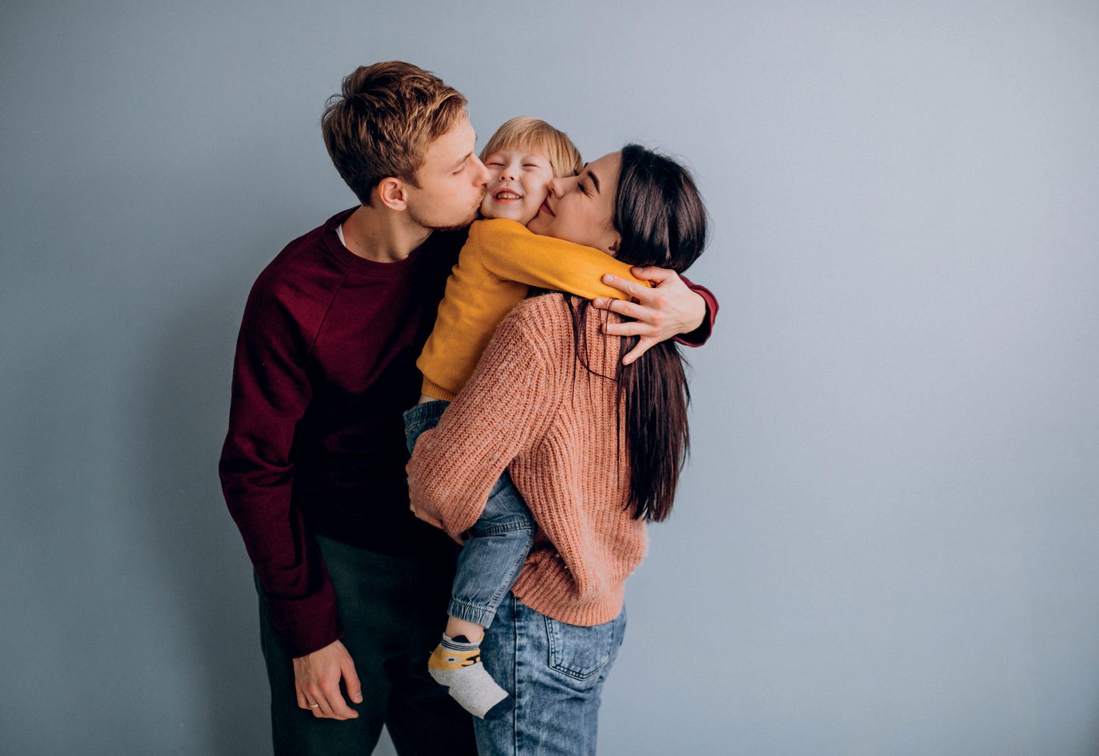 Pais abraçando e beijando o filho pequeno