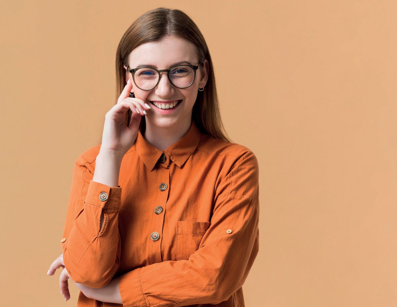 Mulher jovem de óculos sorrindo, com a mão no rosto