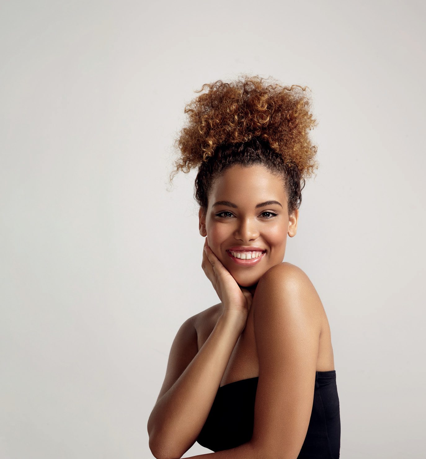 Mulher sorridente de cabelo cacheado com a mão no rosto