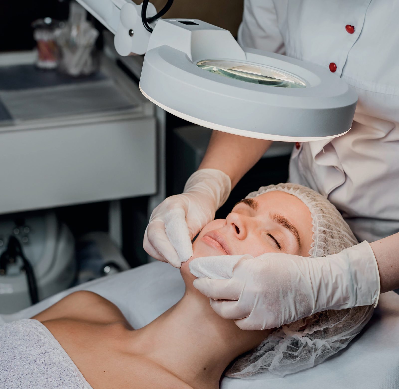 Profissional de luvas realizando procedimento facial em paciente deitada