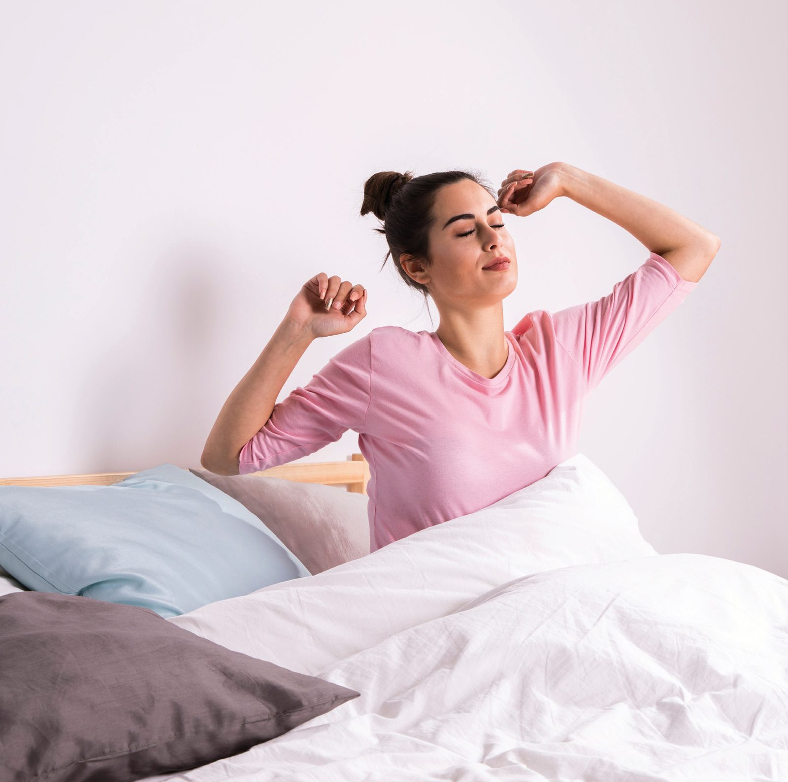 Mulher de blusa rosa se espreguiçando ao acordar, de olhos fechados