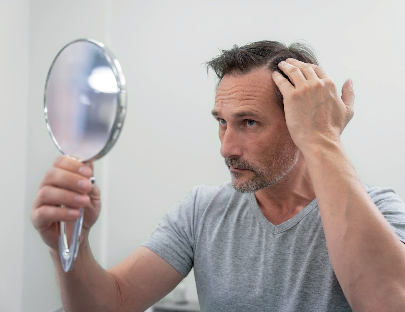 Homem de cabelos grisalhos observando a raiz do cabelo em um espelho de mão